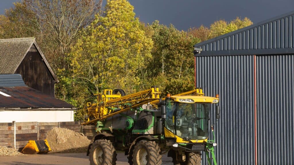 Storm clouds gathering over a self-propelled sprayer in a field.